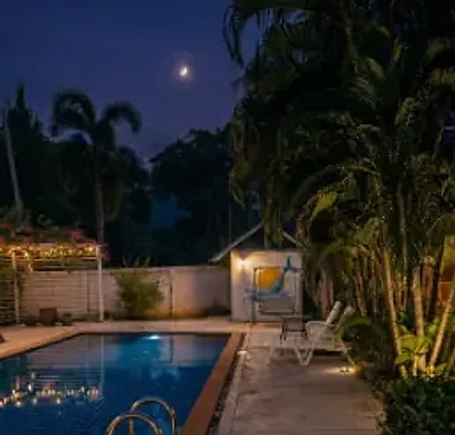 The pool lit up at night under a crescent moon
